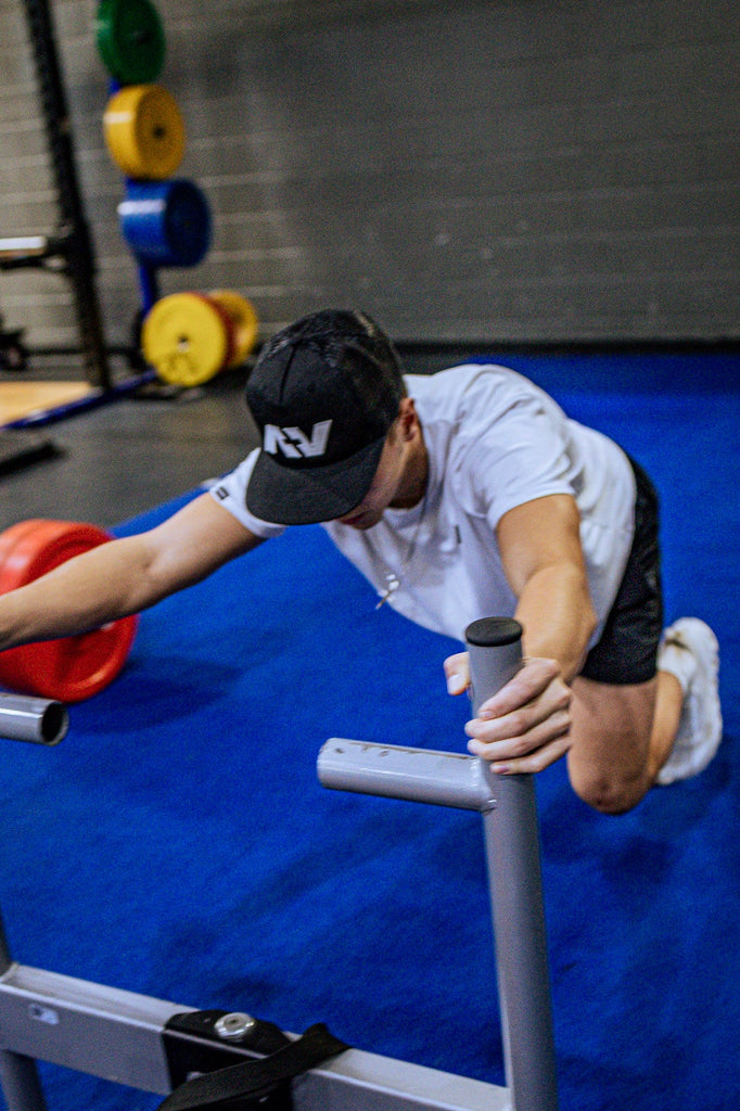 Person using a weight machine in a gym setting with weights and gym equipment in the background.