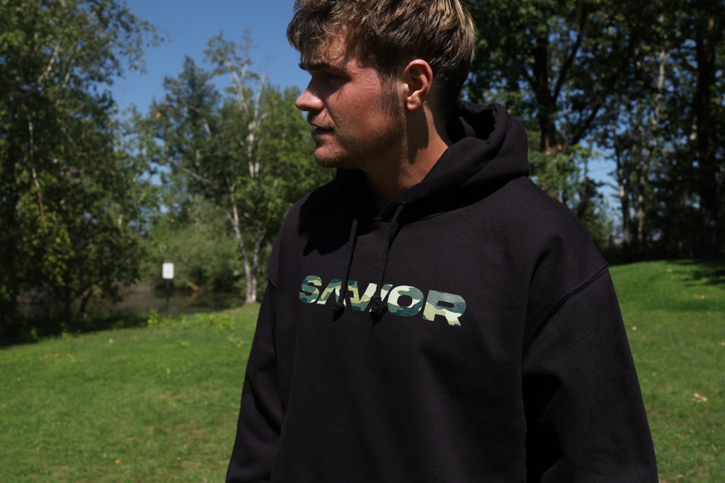Person wearing a black hoodie with 'SAVIOR' text outdoors