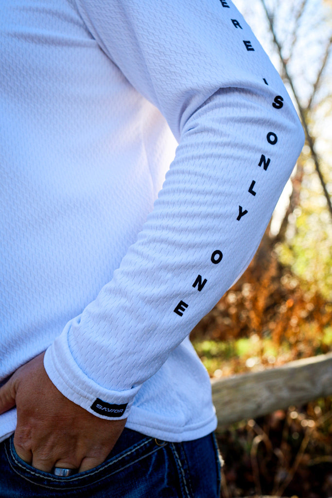 White long-sleeve shirt with text on sleeve against a blurred natural background