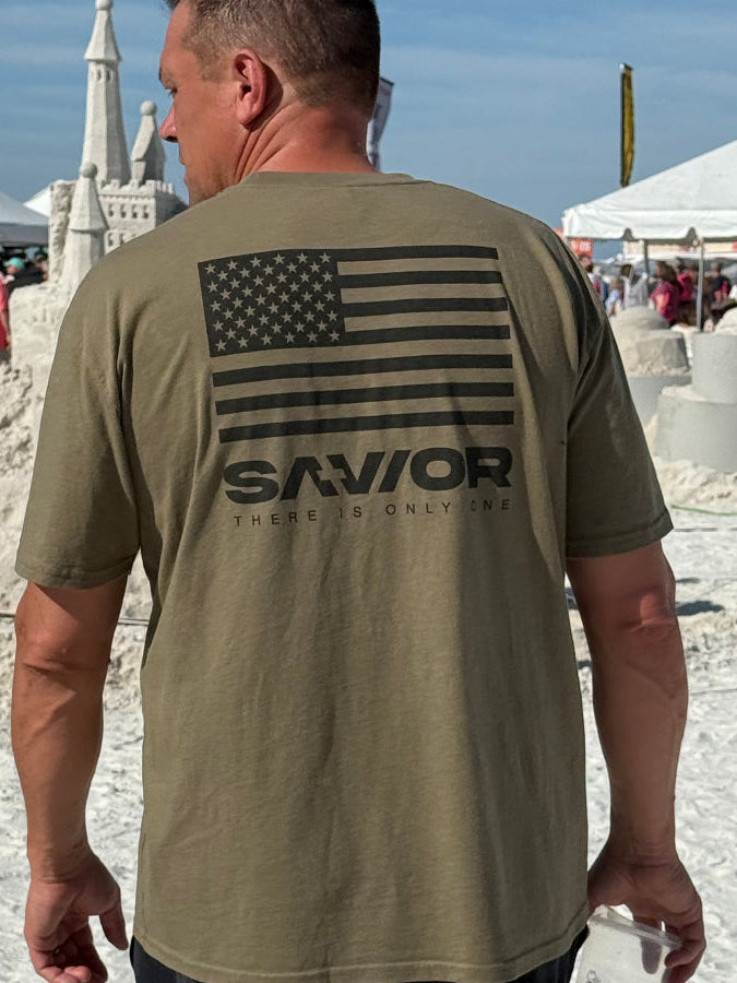 Person wearing a beige t-shirt with a logo and text, standing on a stone surface.