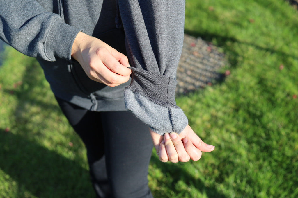 Person adjusting a gray jacket outdoors on a grassy area