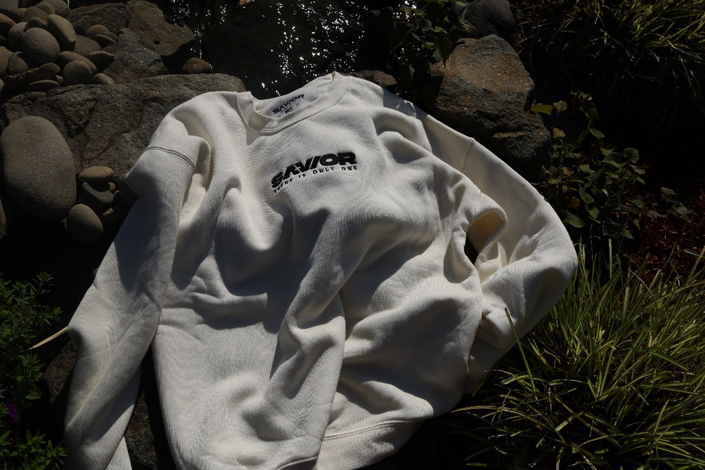 White sweatshirt with text on it lying on grass and rocks