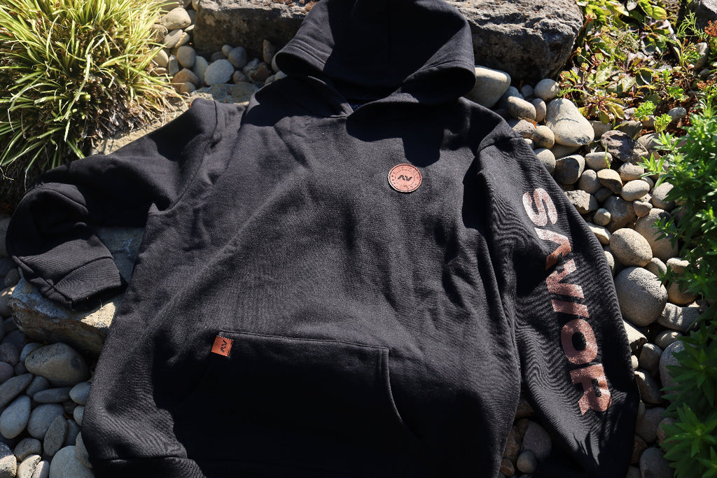 Black hoodie with 'Swarovski' branding on a stone surface with plants.