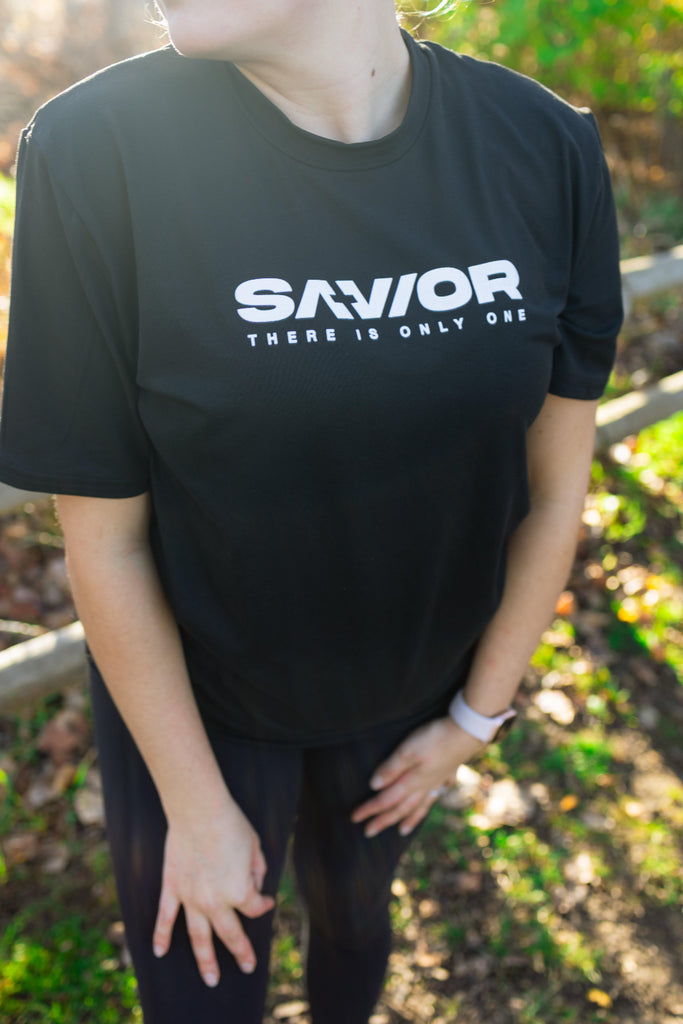 Person wearing a black t-shirt with 'SAVIOR THERE IS ONLY ONE' text outdoors.