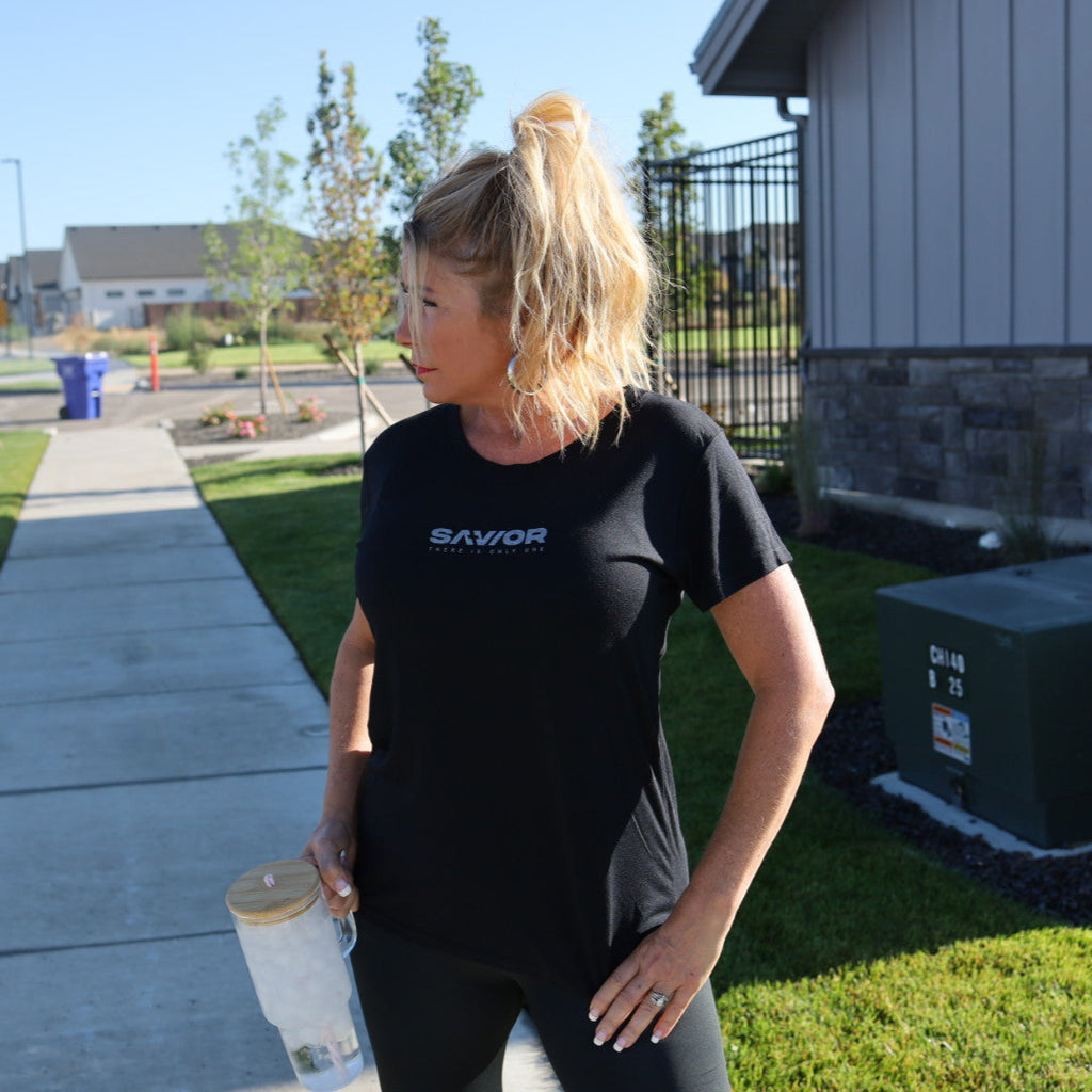 Woman in black t-shirt with 'Savor' logo holding a paint can on a sidewalk.
